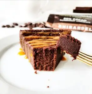 A slice of rich Flourless Chocolate Torte on a dessert plate with a dusting of cocoa powder and fresh raspberries.