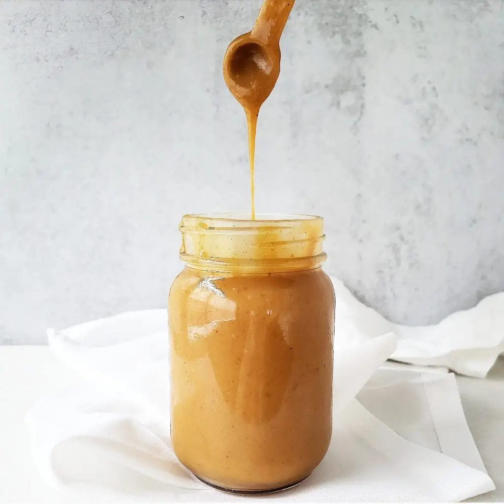 A spoon drizzling the thick, spiced pumpkin caramel sauce over a scoop of vanilla ice cream.