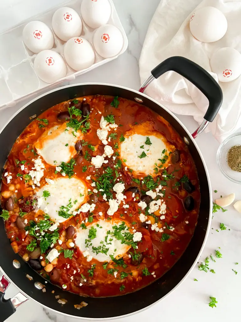 Traditional Shakshuka in a skillet with poached eggs, crumbled feta cheese, and fresh parsley — Sugar Face Bakes