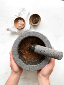 Grinding toasted pumpkin seeds with salt and peppercorns in a molcajete