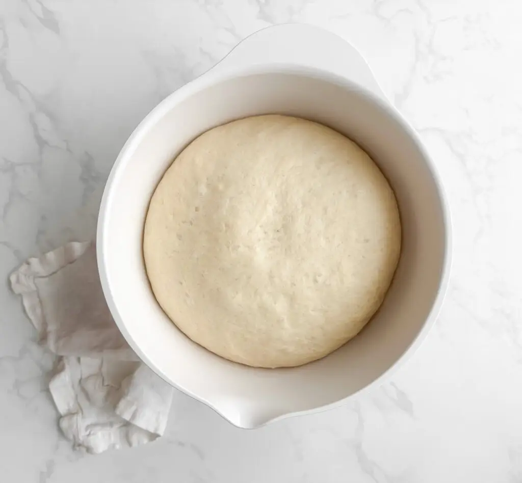 Close-up of hands pressing fingers into proofed focaccia dough to create signature dimples.