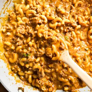 homemade hamburger helper in a one pot skillet with ground beef, macaroni, and melted cheddar cheese