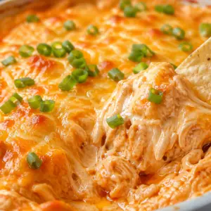 Close-up of creamy buffalo chicken dip with melted cheese and shredded chicken being scooped with a tortilla chip, topped with green onions