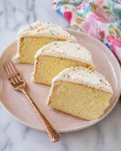 Eggless vanilla cake slices on a pink ceramic plate with rose gold fork, soft moist crumb and light buttercream frosting with sprinkles
