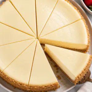 Overhead close-up view of a sliced creamy cheesecake with one slice being removed from the whole cheesecake.