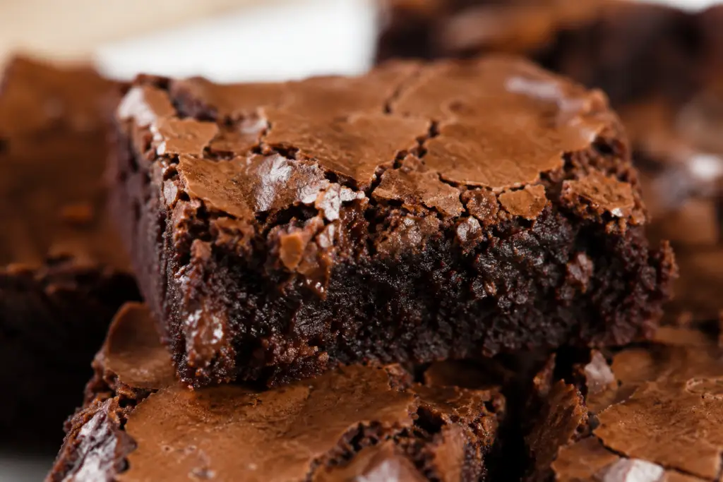 Close-up of a homemade fudgy brownie without chocolate chips in the batter, with a thin crackly top, gooey chocolate center, and flaky sea salt sprinkled over the glossy surface.