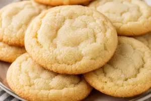 Close-up of soft and chewy sugar cookies with lightly golden edges and tender centers, stacked on a plate and coated in sparkling sugar.