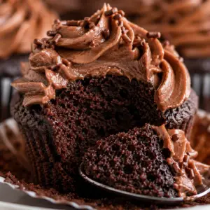 - Chocolate Cupcakes Recipe Close-up of a moist chocolate cupcake with the wrapper peeled down and a spoonful removed from the front, revealing a rich, tender chocolate crumb beneath silky chocolate buttercream frosting.