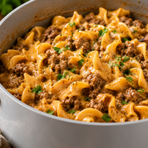 - One Pot Ground Beef and Noodles with Beef Broth Close-up of creamy one-pot ground beef and egg noodles cooked in a white Caraway-style Dutch oven with a light gray ceramic interior, garnished with parsley and black pepper on a rustic wooden table.