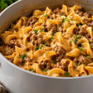 Close-up of creamy one-pot ground beef and egg noodles cooked in a white Caraway-style Dutch oven with a light gray ceramic interior, garnished with parsley and black pepper on a rustic wooden table.