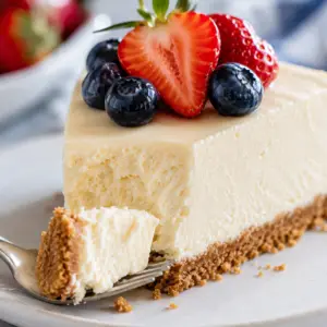 no bake cheesecake- No-Bake Cheesecake Recipe Close-up of a slice of creamy no-bake cheesecake with a forkful removed from the tip, revealing its light, silky texture and buttery graham cracker crust, topped with fresh strawberries and blueberries.