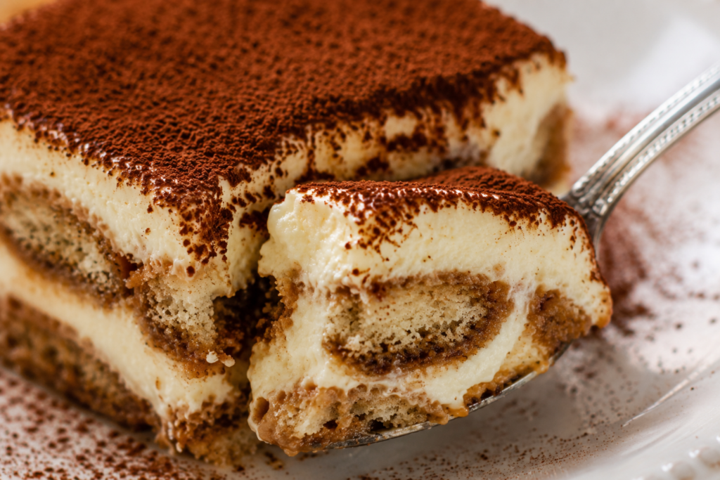 Close-up of a spoon lifting a creamy bite of homemade tiramisu, revealing soft espresso-soaked ladyfingers and smooth mascarpone filling.