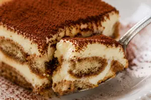 Close-up of a spoon lifting a creamy bite of homemade tiramisu, revealing soft espresso-soaked ladyfingers and smooth mascarpone filling.