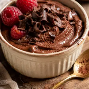 cottage cheese chocolate mousse- Cottage Cheese Chocolate Mousse Close-up of creamy cottage cheese chocolate mousse in a rustic ceramic ramekin topped with dark chocolate curls, cocoa powder, flaky sea salt, and fresh raspberries.