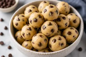 Bowl of homemade eggless edible cookie dough balls with mini chocolate chips, including a gooey cookie dough ball cut open to show the soft creamy center.