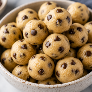 Bowl of homemade eggless edible cookie dough balls with mini chocolate chips, including a gooey cookie dough ball cut open to show the soft creamy center.