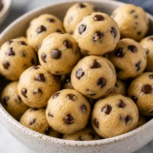 eggless cookie dough- Eggless Cookie Dough Recipe (Safe to Eat!) Bowl of homemade eggless edible cookie dough balls with mini chocolate chips, including a gooey cookie dough ball cut open to show the soft creamy center.