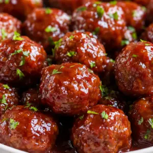 crockpot party meatballs- Crockpot Party Meatballs Close-up of slow cooker party meatballs coated in a glossy grape jelly and chili sauce glaze, served in a white bowl and garnished with fresh parsley.