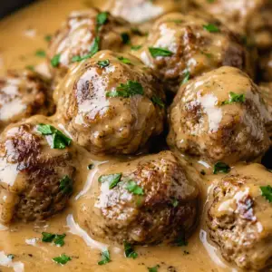 Close-up of homemade Swedish meatballs smothered in rich, creamy brown gravy and garnished with fresh parsley in a skillet.