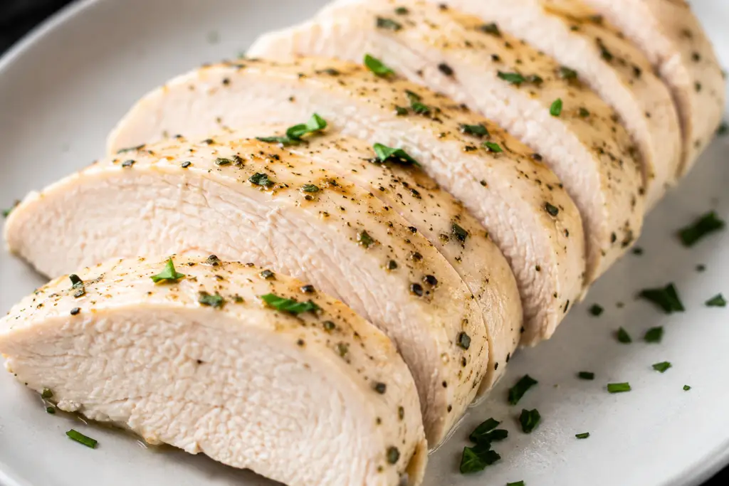 Juicy boiled chicken breast sliced into thick pieces and seasoned with black pepper, garlic, and fresh herbs on a plate.