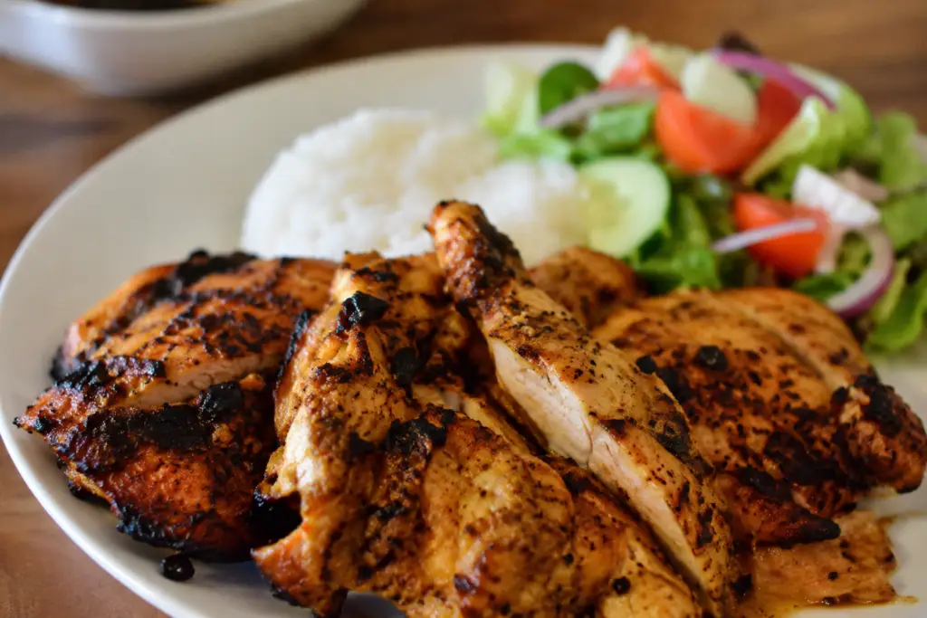 Juicy marinated grilled chicken served with white rice and a fresh cucumber, tomato, and lettuce salad.